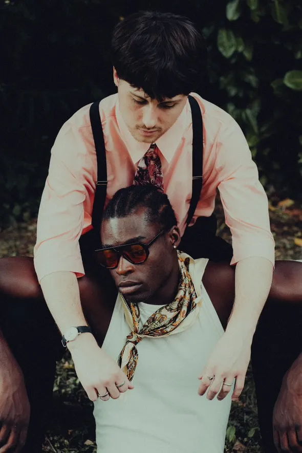 Deux modèles superposés, l'un en chemise rose et bretelles, l'autre en débardeur blanc, foulard et lunettes noires.