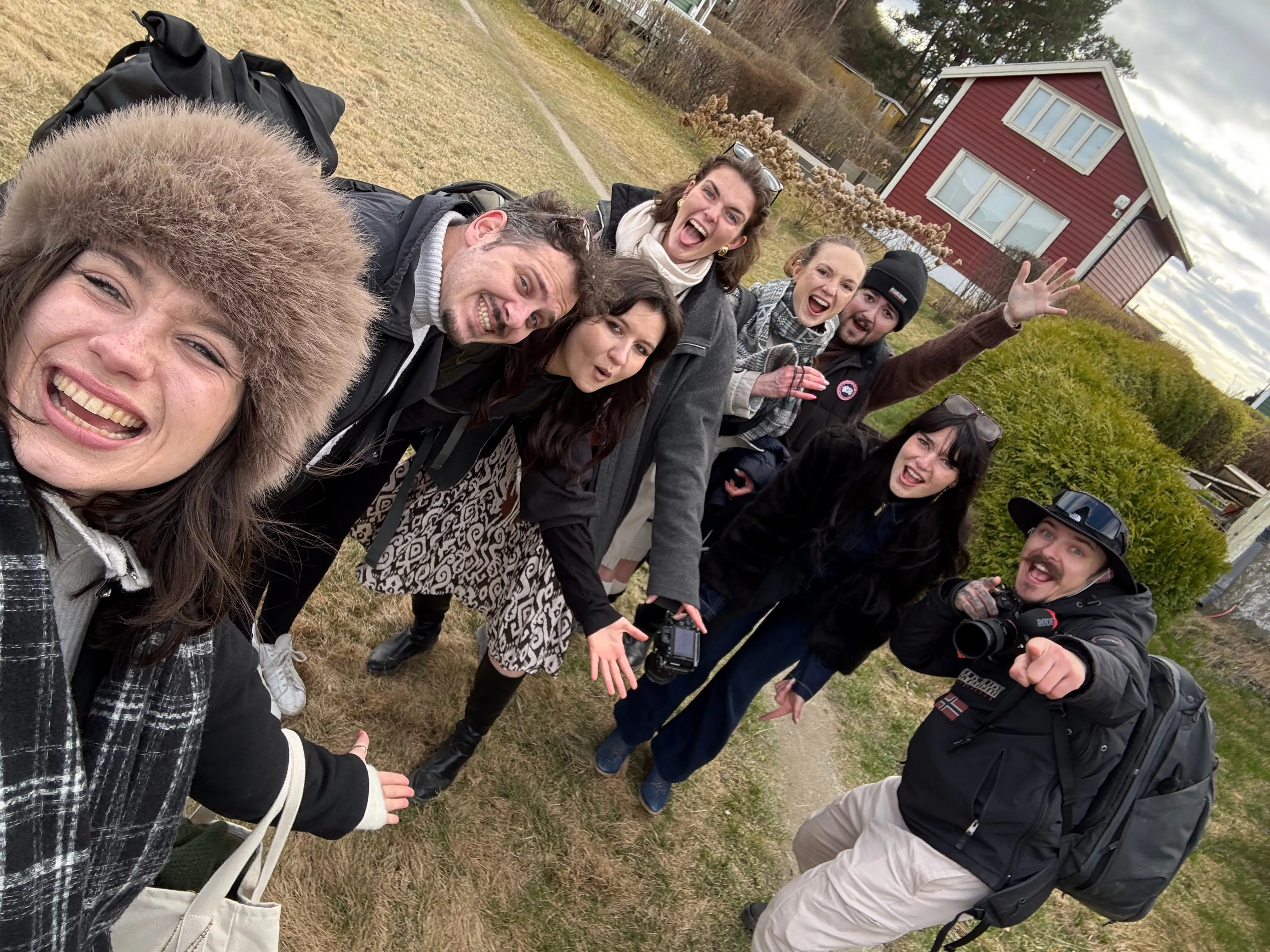 Selfie joyeux du groupe sur une pelouse, devant une maison norvégienne en bois rouge.