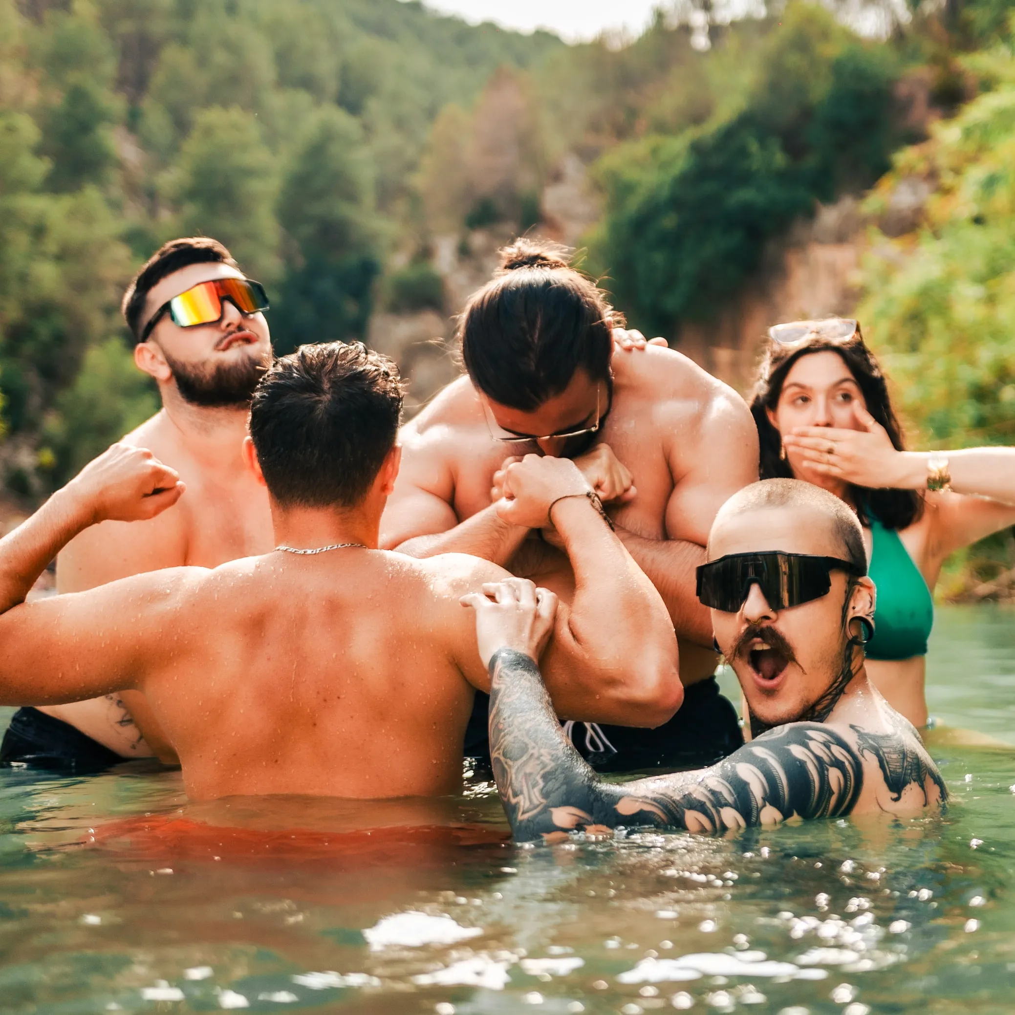 Un groupe de modèles rit et chahute dans l'eau d'une rivière entourée de collines boisées.