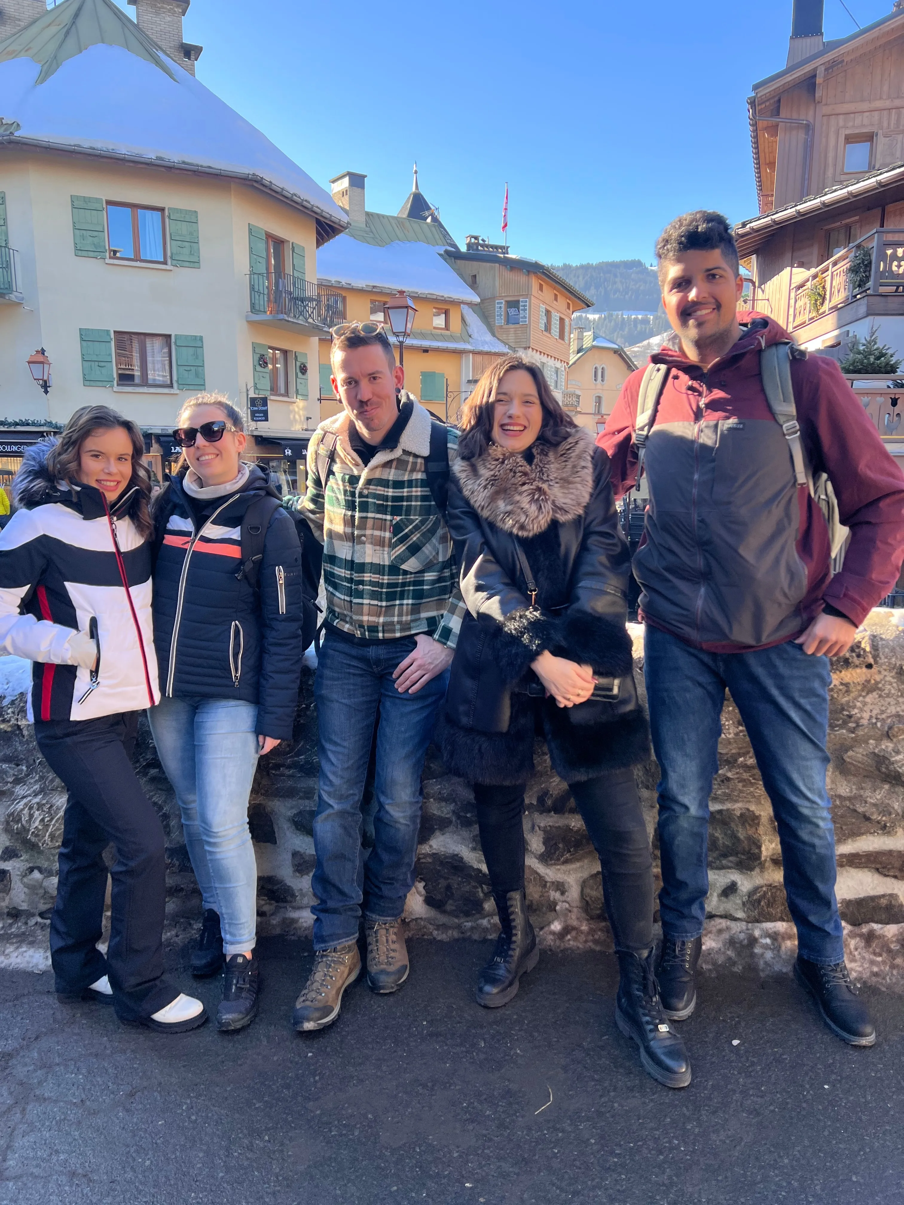 Le groupe pose sur un muret devant les chalets du village de Megève, sous un ciel bleu.