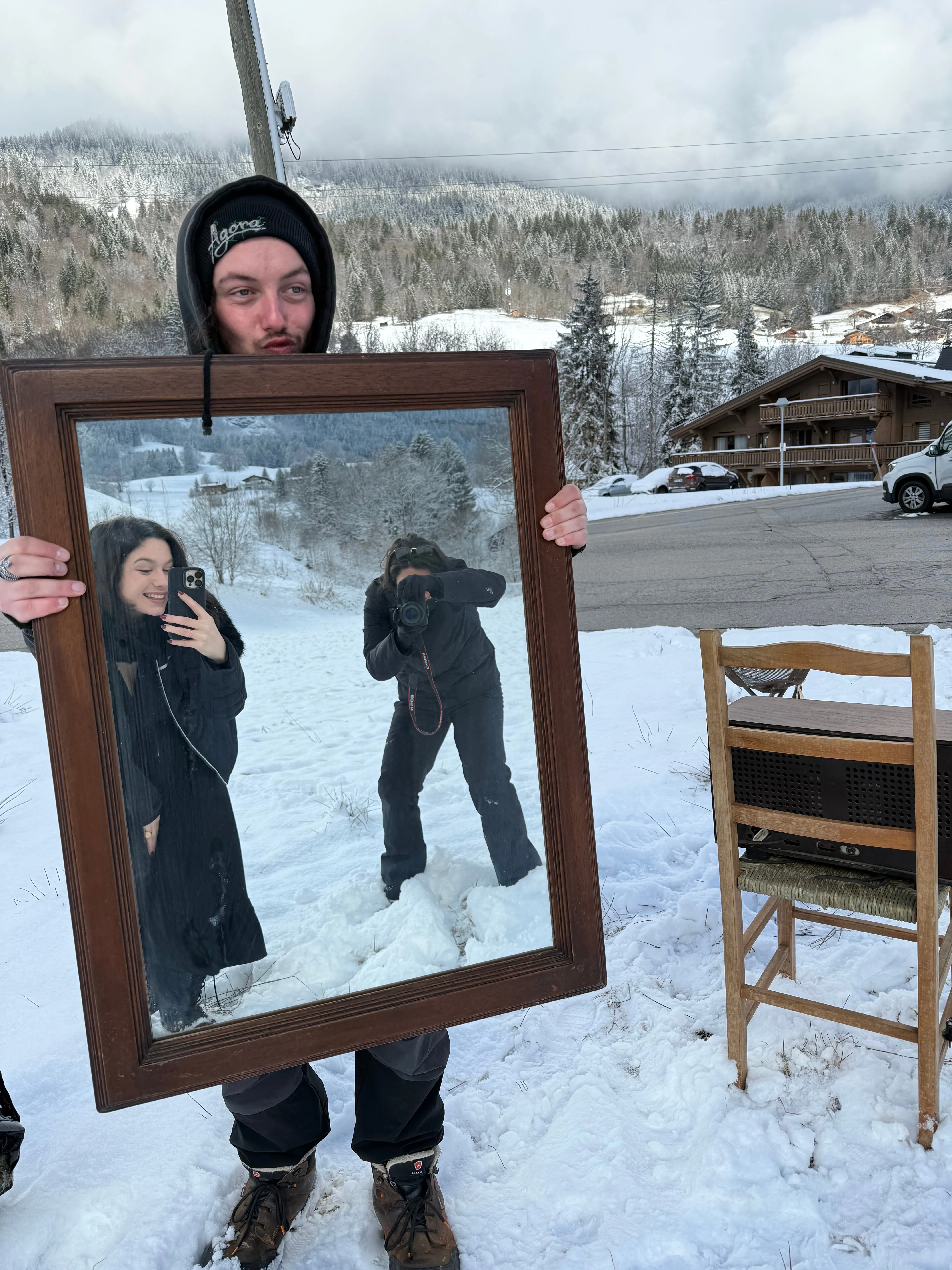 Un participant tient un grand miroir ancien dans la neige, qui reflète une modèle et un photographe.
