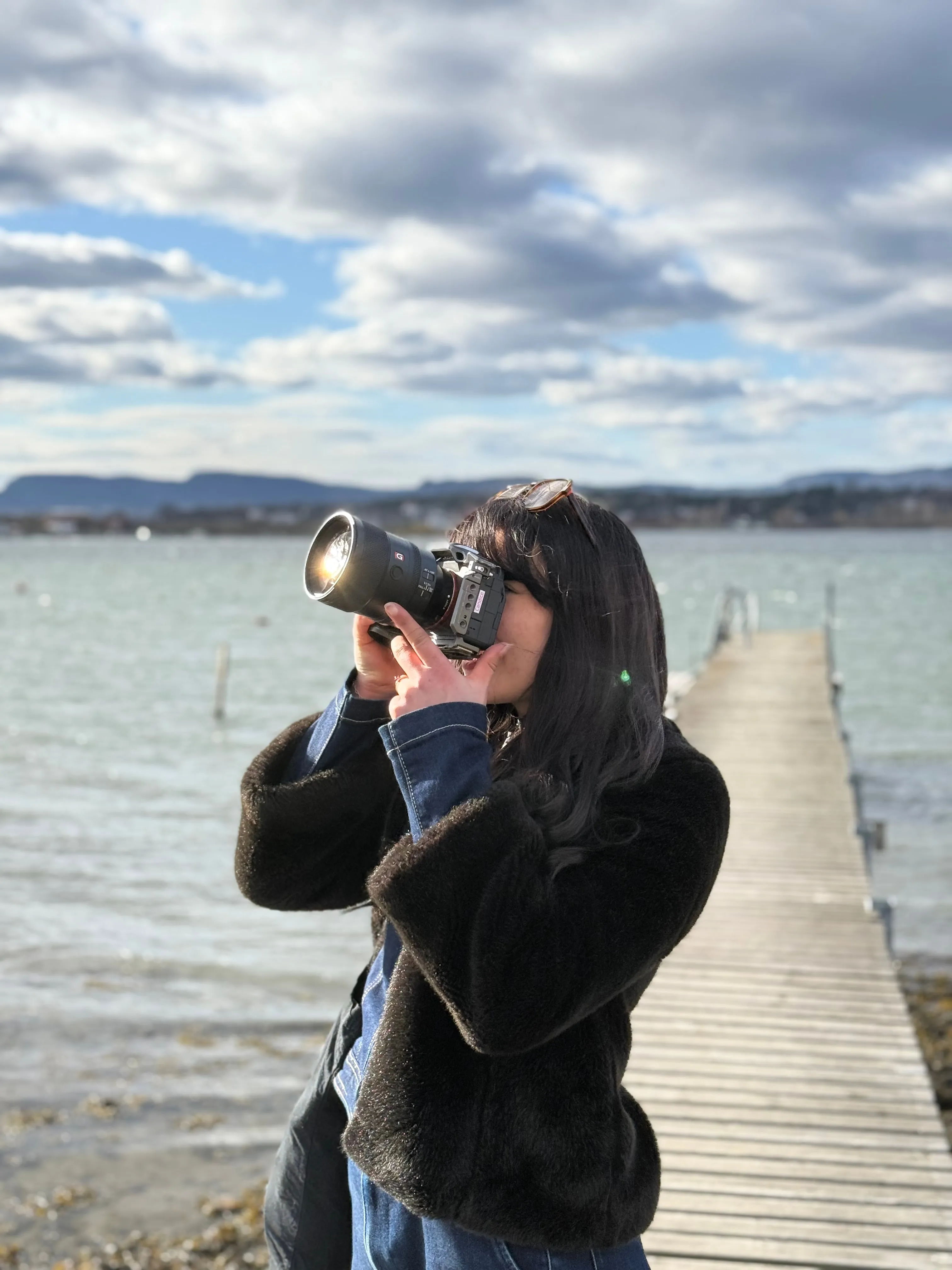 Une photographe cadre à l'objectif au bout d'un ponton en bois, face au fjord d'Oslo.