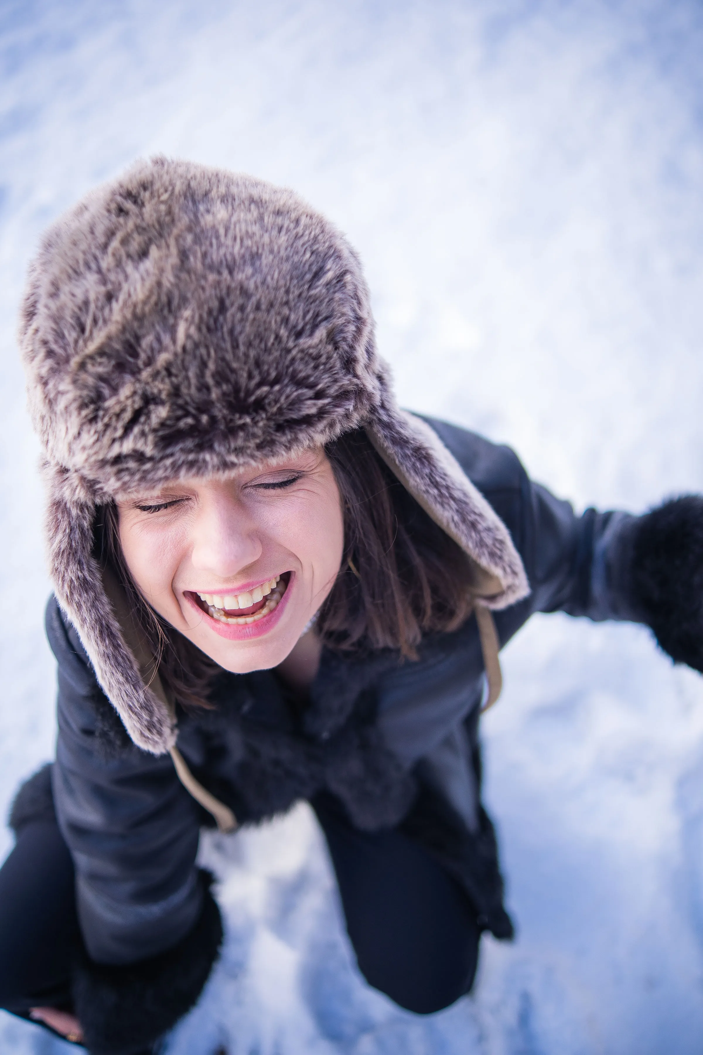 Une participante en chapka éclate de rire, penchée vers l'objectif dans la neige.
