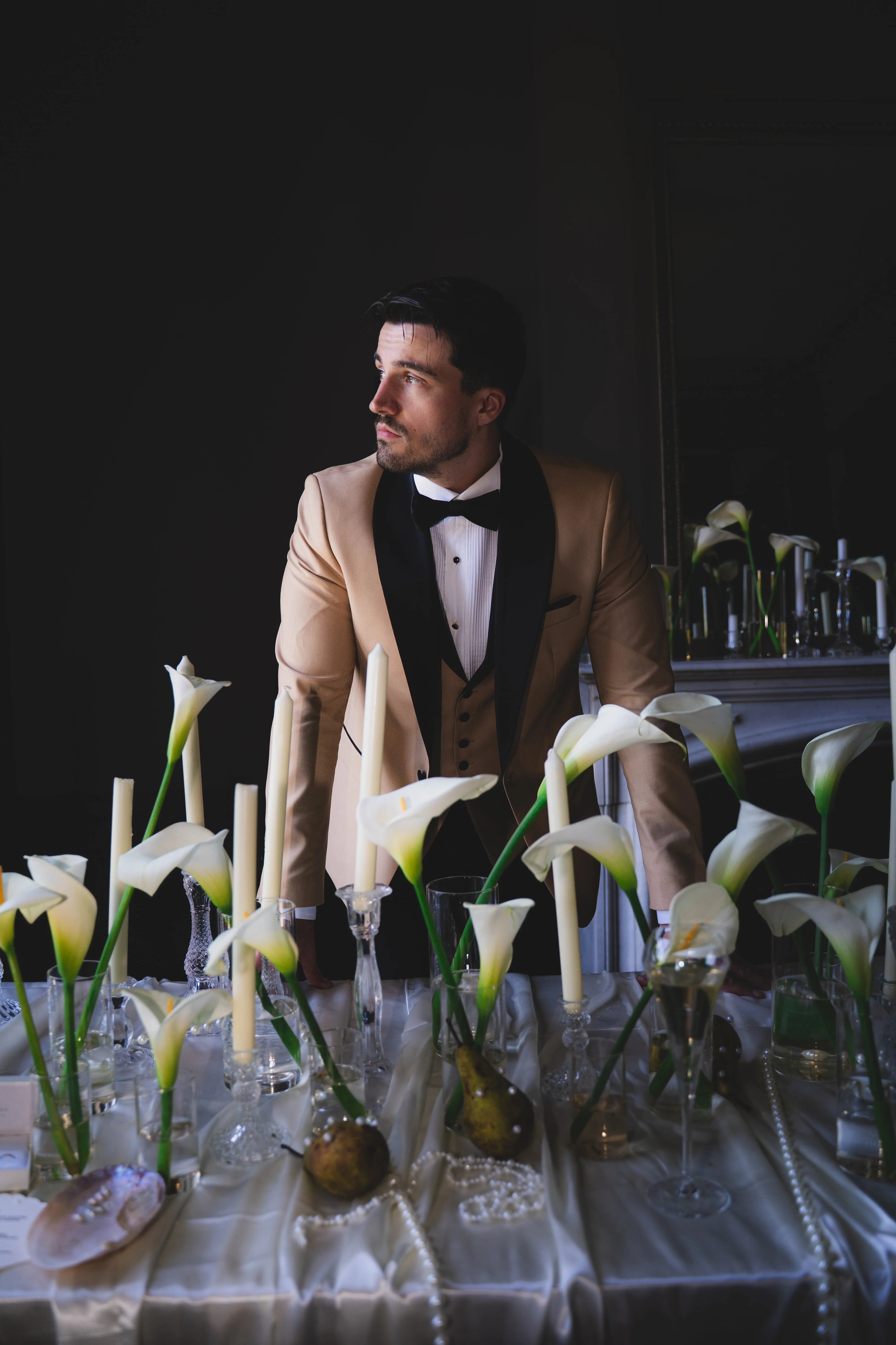 Portrait d'un marié en smoking champagne, derrière une table dressée d'arums et de bougies.