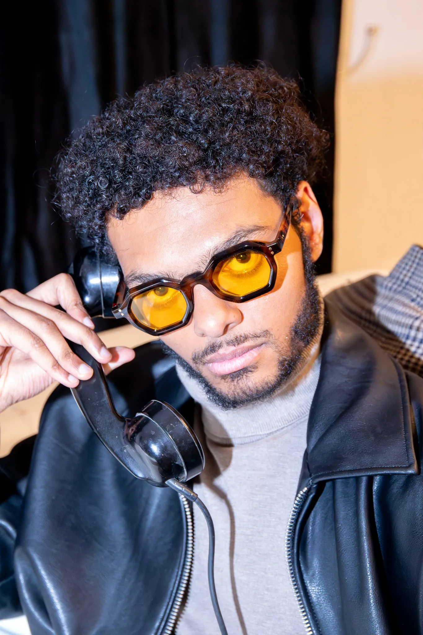 Un modèle en blouson de cuir et lunettes jaunes tient le combiné d'un téléphone rétro.