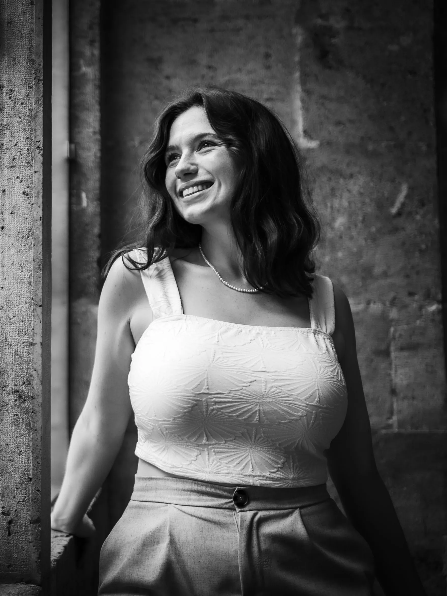 Portrait en noir et blanc d'une modèle souriante en bustier blanc, près d'une porte en pierre.