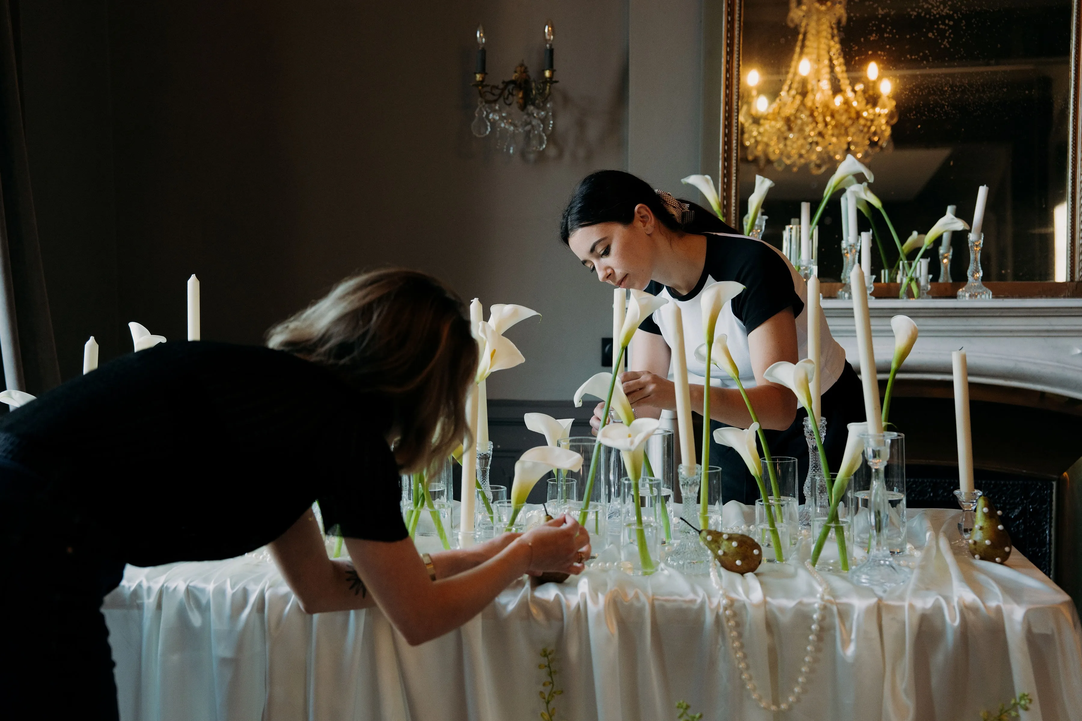 Deux membres de l'équipe installent les arums et les bougies sur la table des salons, sous un lustre en cristal.