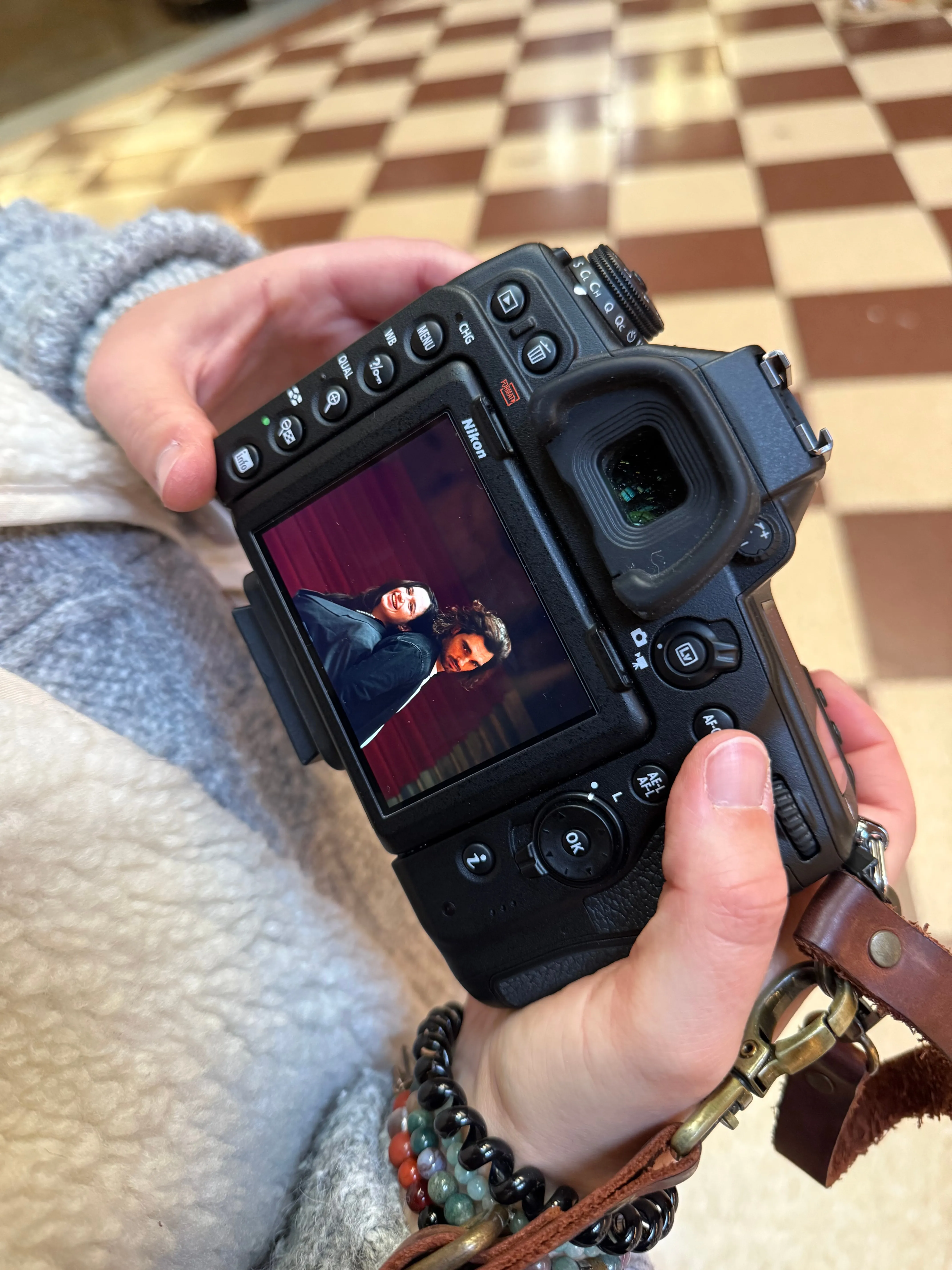 Une photographe vérifie un portrait sur l'écran de son appareil, au-dessus d'un sol en damier.
