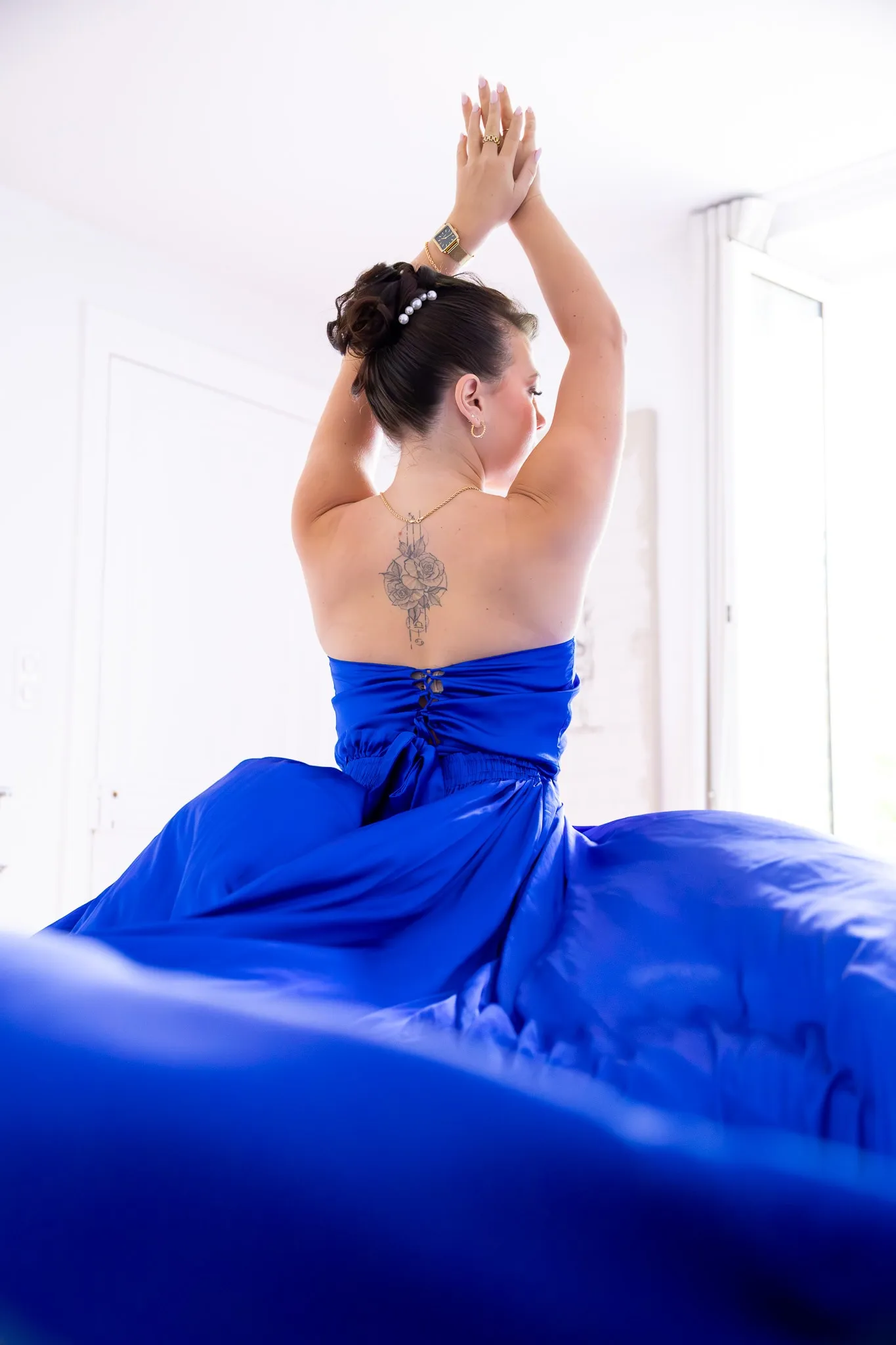 Une modèle de dos, mains jointes au-dessus de la tête, dans une robe bleu roi drapée.