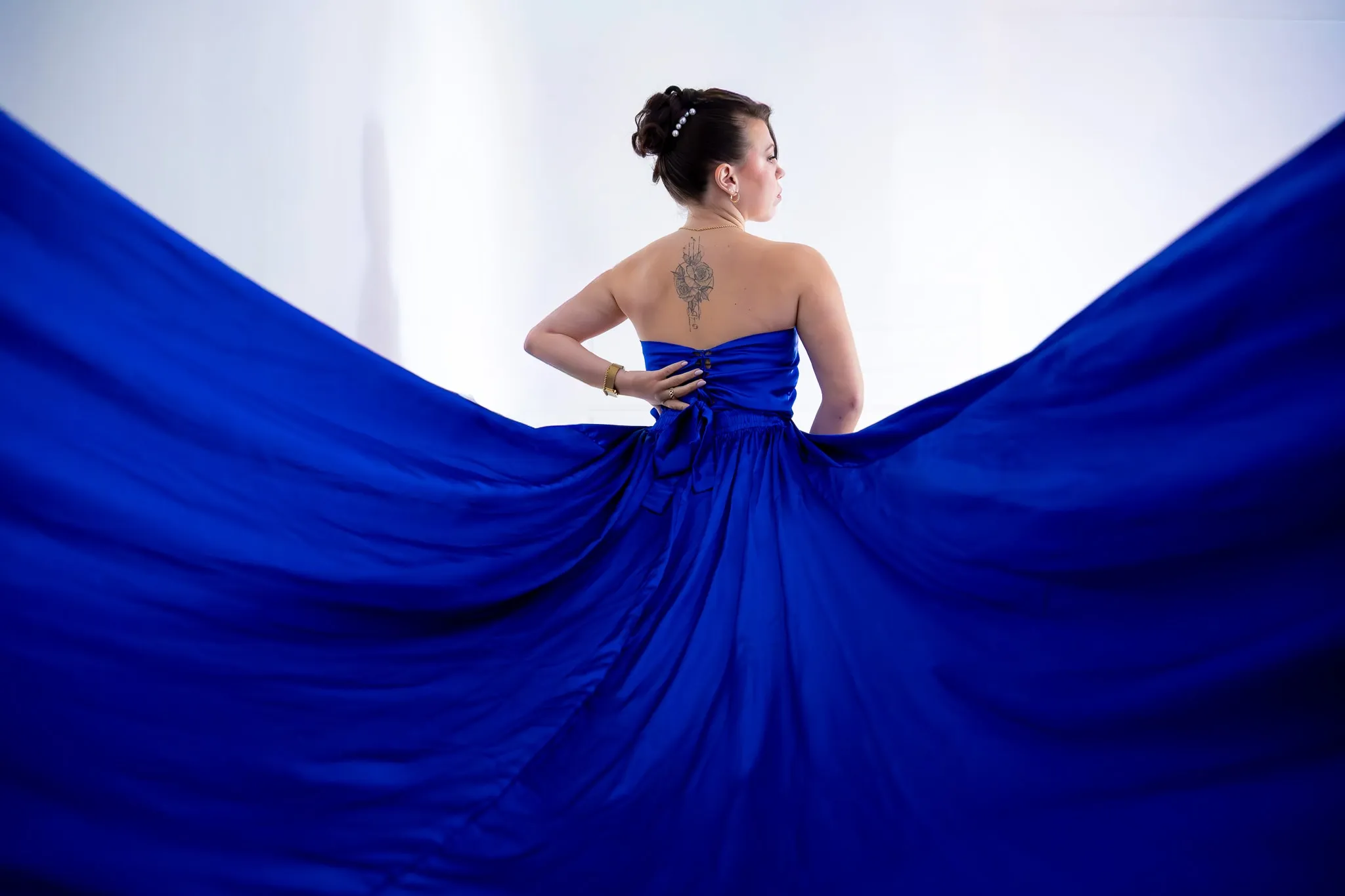 Une modèle de dos dans une robe bleu roi, la traîne déployée en éventail sur fond blanc.