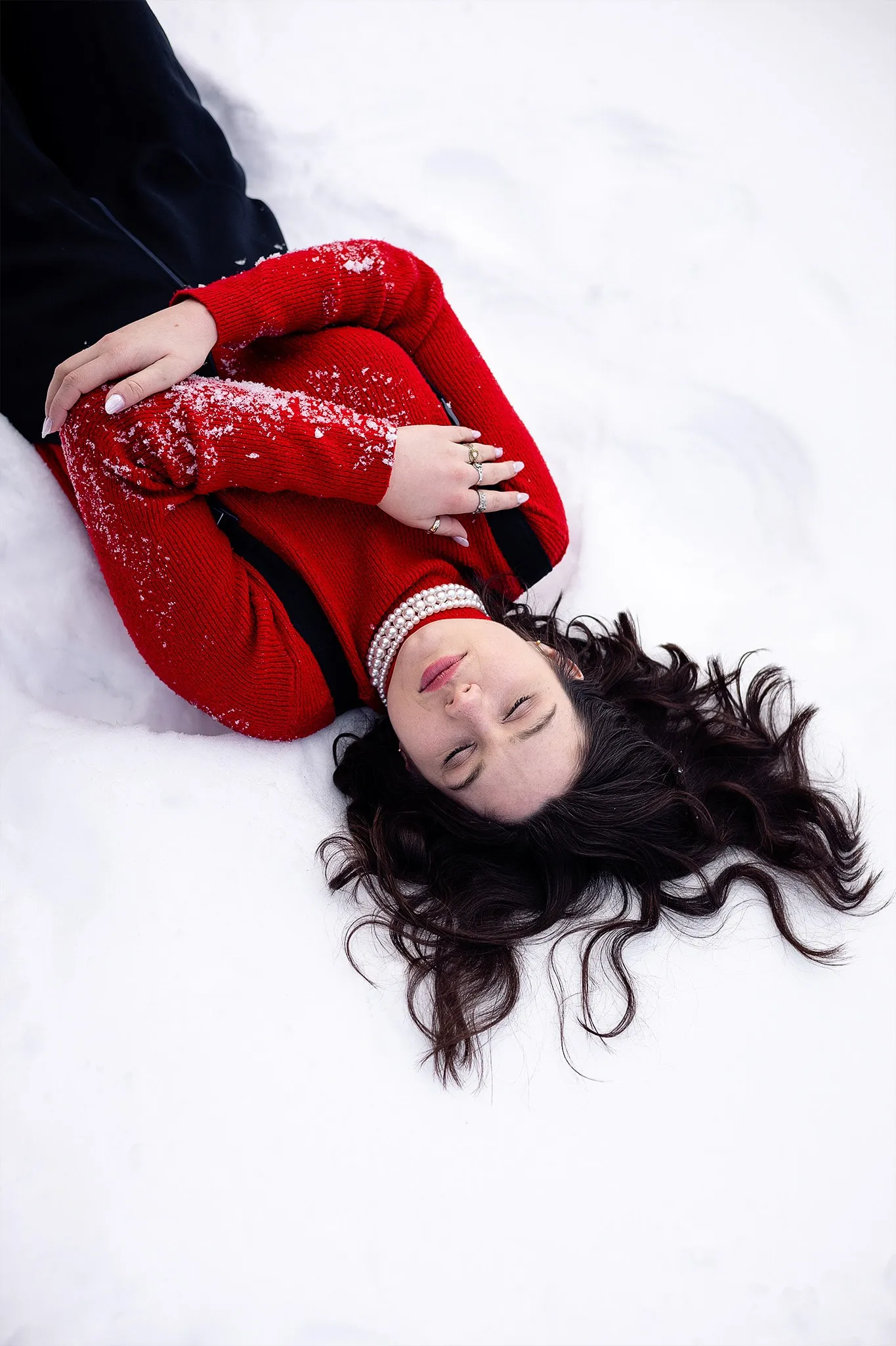 Une modèle en robe rouge pailletée allongée dans la neige, cheveux étalés autour d'elle.