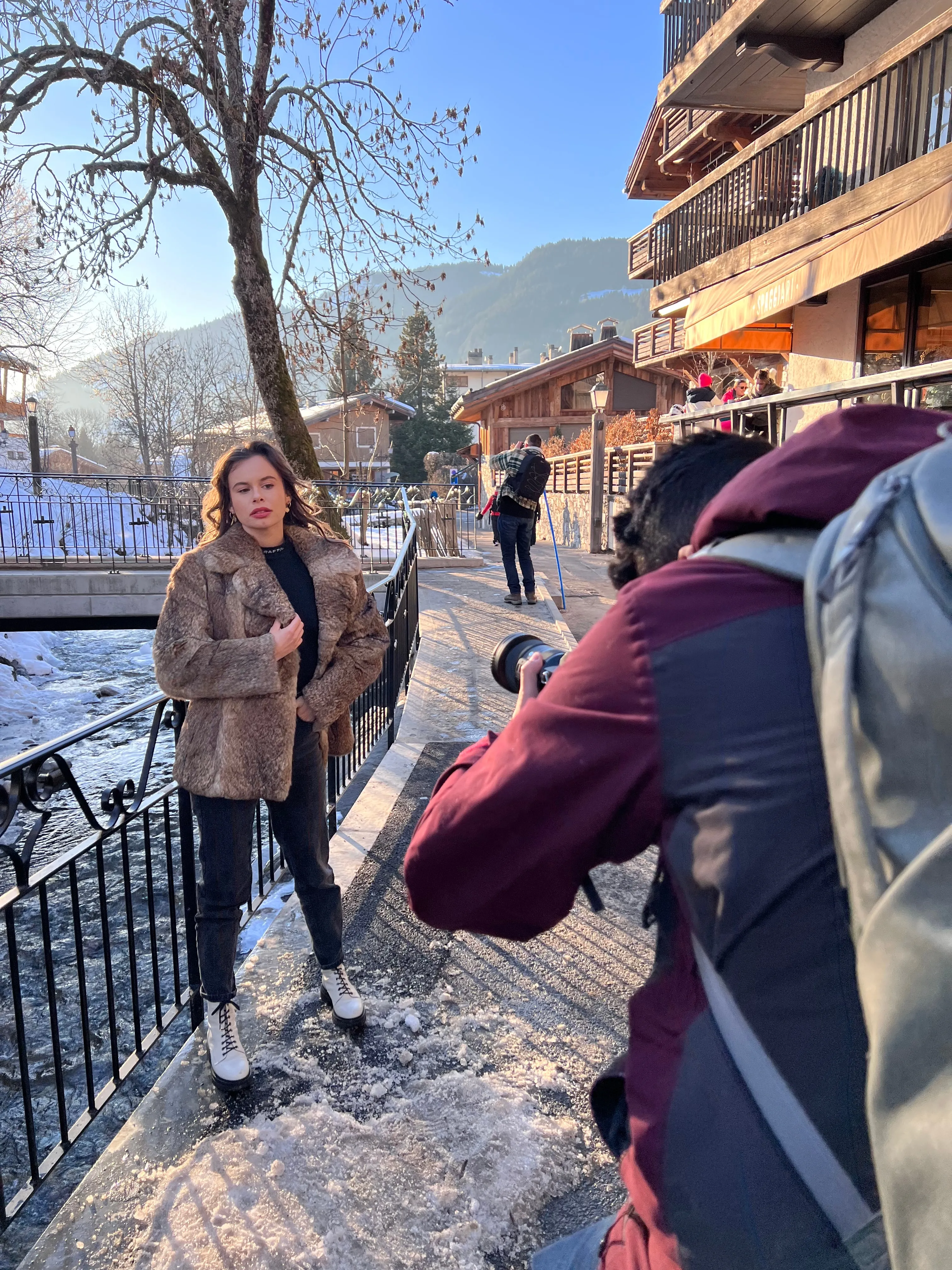 Un photographe shoote une modèle en manteau de fourrure sur un pont au-dessus du torrent de Megève.
