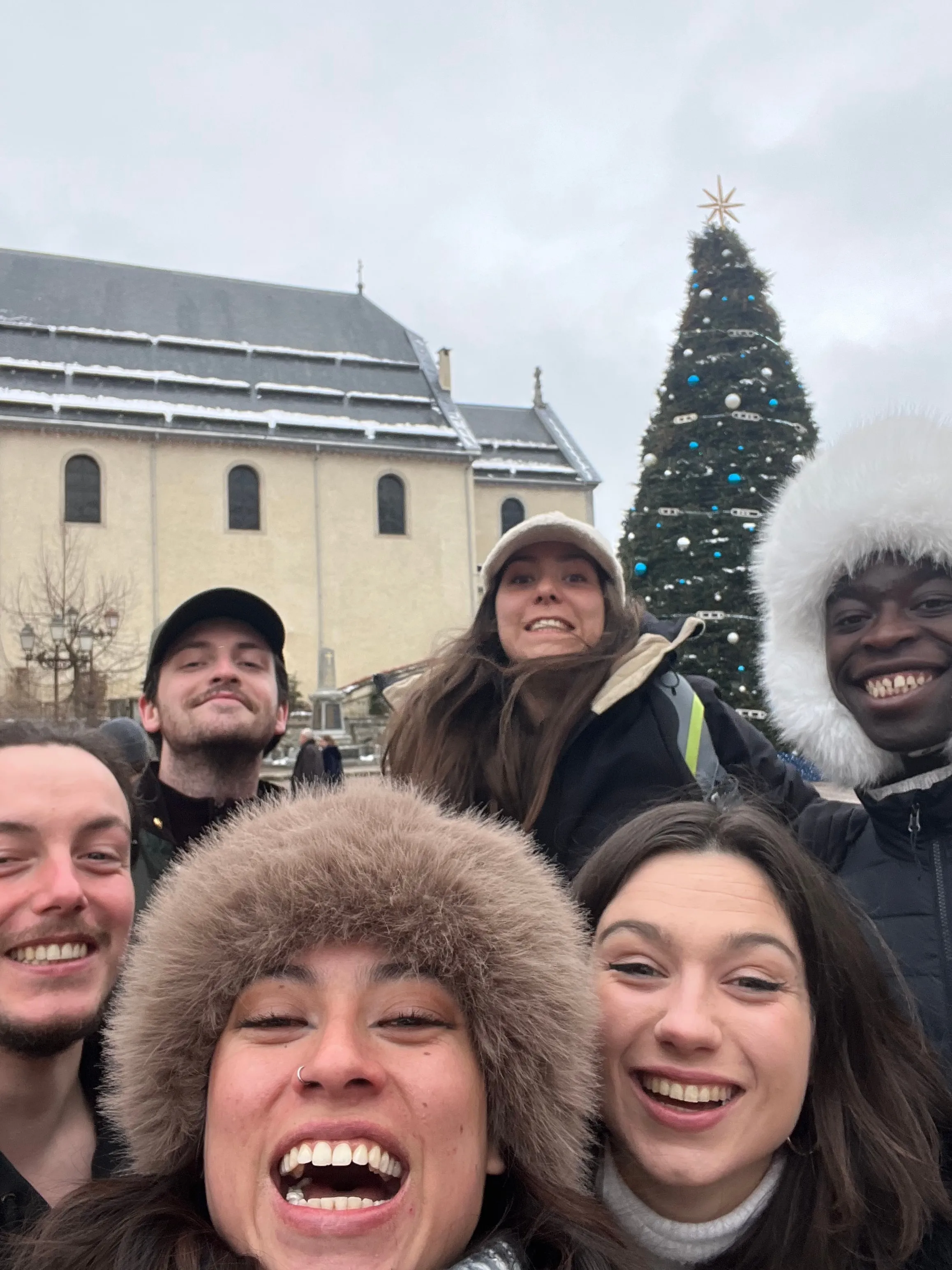 Selfie joyeux du groupe emmitouflé devant l'église et le sapin de Noël de Megève.