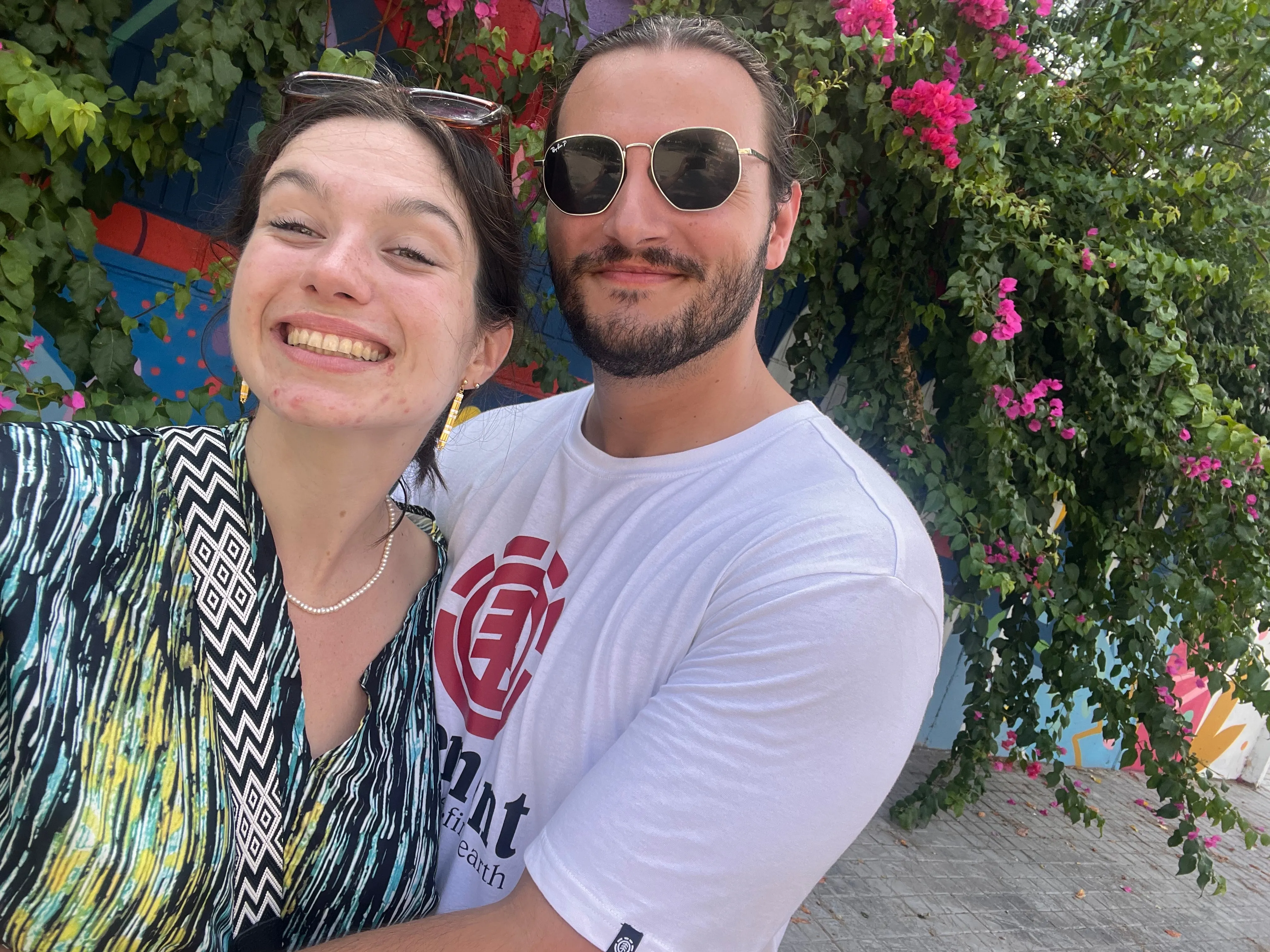 Selfie de deux participants devant un massif de bougainvilliers roses.