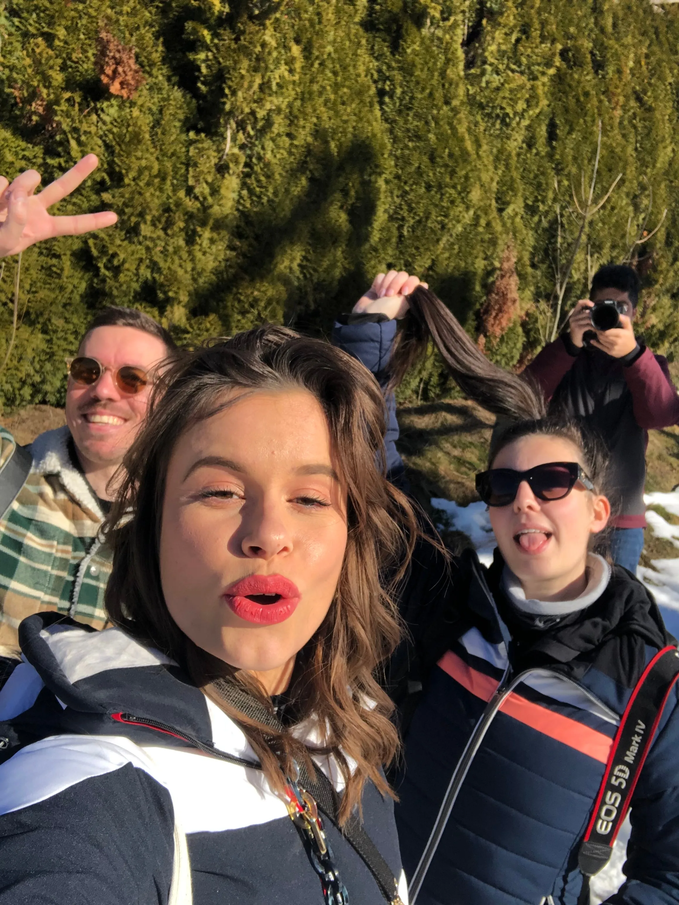 Selfie d'une participante au rouge à lèvres rouge avec le groupe et un photographe derrière elle, au soleil.